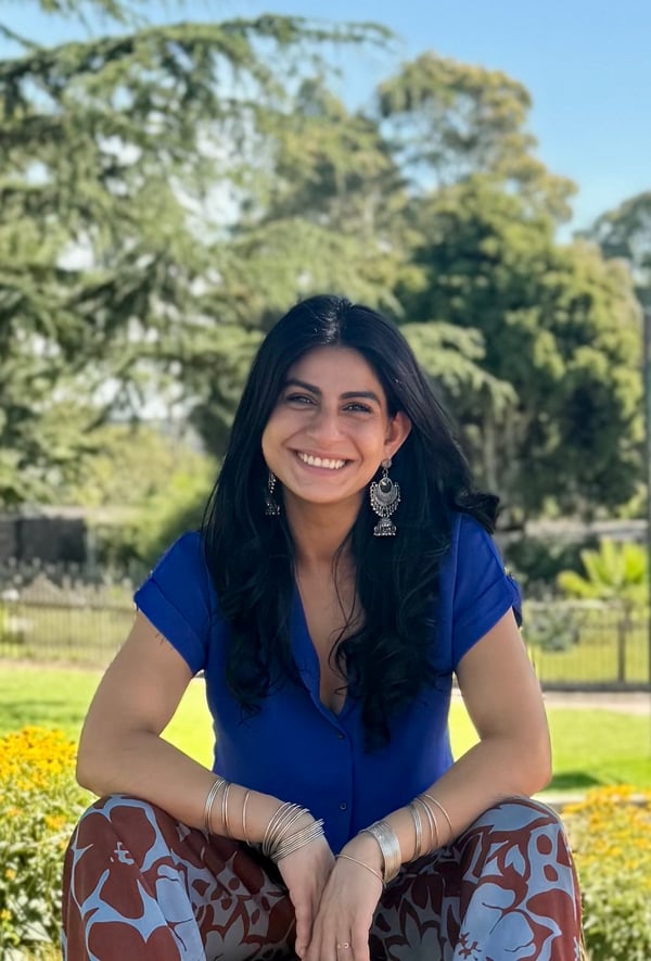 Zara Grewal, founder of Copper Kettle Consulting, smiling while sitting outdoors in a sunny garden, wearing a bright blue shirt, patterned trousers, and silver Pakistani bangles with jhumka earrings. Zara Grewal, founder of Copper Kettle Consulting, smiling while sitting outdoors in a sunny garden, wearing a bright blue shirt, patterned trousers, and silver Pakistani bangles with jhumka earrings.